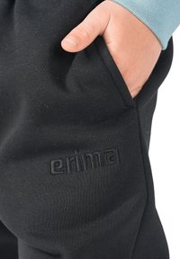 Zwarte sweatpants met een zachte textuur en een voorzak. Voorzien van een geperst "erima"-logo. Afgewerkt met boorden bij de enkels.
