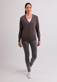 Grå knapp-up cardigan i mjukt stickat material, V-ringad design, långa ärmar, med en avslappnad passform, tillsammans med grå slim jeans och vita sneakers.