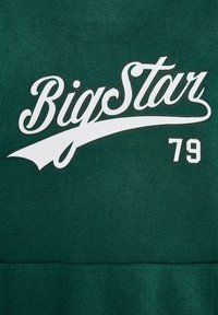 Zelena dukserica s bijelim natpisom "Big Star" i brojem "79." Mekana tkanina s glatkom teksturom, klasični dizajn s okruglim izrezom.