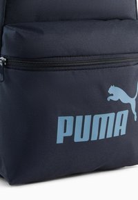 Marinblå ryggsäck tillverkad av slitstarkt tyg, med en framficka med dragkedja och Puma-logga i ljusblått. Strukturerad yta med förstärkt sömnad.