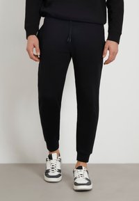 Zwarte sweatpants van zachte stof met een elastische tailleband en een trekkoord. Tapered fit met ribgebreide boorden en zijzakken.