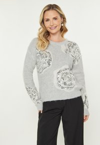 Maglione grigio in maglia con motivi floreali di paillettes, dotato di maniche lunghe e colletto rotondo. Texture morbida e vestibilità rilassata. Indossati pantaloni neri.