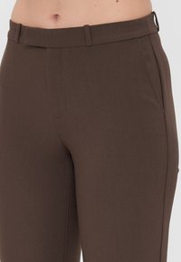 Brune skreddersydde bukser med en jevn tekstur, elegant design og et liv med beltehemper. Inkluderer sidelommer og subtile sømdetaljer.