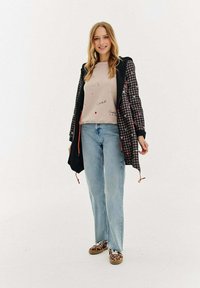 Jauna sieviete, kas valkā pārbauda kapuci ar sirds rakstu, gaiši apdrukātu džemperi, gaiši zila džinsi un leopardu raksta sporta apavus.