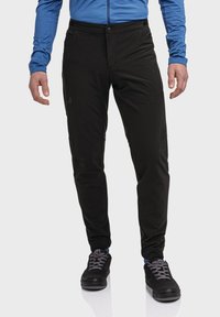 Schwarze Outdoor-Hosen mit glatter Textur, schmaler Passform und Fronttaschen, kombiniert mit schwarzen Schuhen und einem blauen Langarmhemd.