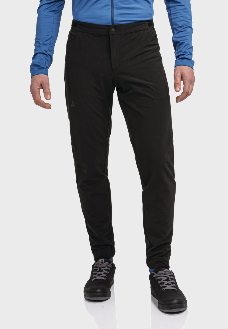 Schwarze Outdoor-Hosen mit glatter Textur, schmaler Passform und Fronttaschen, kombiniert mit schwarzen Schuhen und einem blauen Langarmhemd.