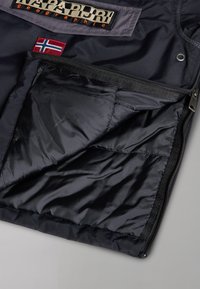 Section de veste Napapijri noire avec poche partiellement dézippée montrant une doublure intérieure matelassée et un écusson du drapeau norvégien.