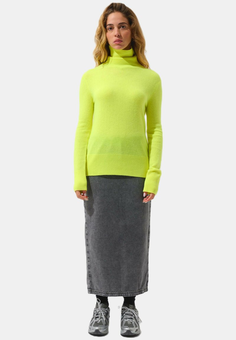 Neon gul polotröja med ribbad nederkant, kombinerad med en lång grå denimkjol och grå sneakers. Enkla, moderna designelement.