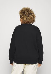 Černá mikina s kulatým výstřihem a spadlými rameny, s žebrovanými manžetami a lemem, vyrobená z měkké, strukturované tkaniny.