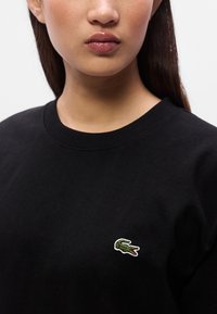 Μαύρο βαμβακερό φούτερ με στρογγυλή λαιμόκοψη και μικρό πράσινο κεντημένο λογότυπο κροκοδείλου στο αριστερό στήθος. Λείο ύφασμα.