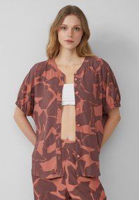 Bruine en oranje gestreepte shirt met een ronde hals, korte pofmouwen en knoopsluiting aan de voorkant, gemaakt van lichte stof.