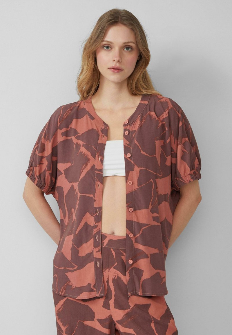 Bruine en oranje gestreepte shirt met een ronde hals, korte pofmouwen en knoopsluiting aan de voorkant, gemaakt van lichte stof.