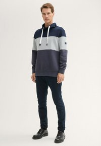 Sudadera con bloque de color en azul marino y gris, con cordones, puños y dobladillo de canalé; combinada con pantalones oscuros y zapatos negros.