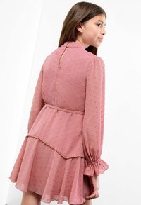 Rotes Kleid aus strukturiertem Stoff mit kleinen Puffpunkten, langen Ärmeln mit voluminösen Manschetten, tailliertem Schnitt und Schlüssellochverschluss im Rücken.