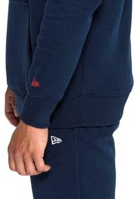 Completo felpa e pantaloni blu navy. Il pullover presenta un logo rosso sulla manica; i pantaloni hanno un logo bianco sul lato, realizzati in morbido tessuto.