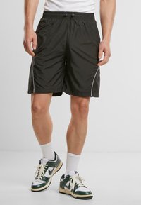 Shorts de sport noirs avec une taille élastique, un cordon de serrage, des accents blancs sur les côtés et une texture légère et lisse.