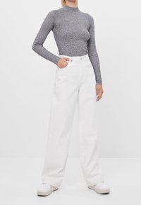 Szary prążkowany top z długim rękawem w połączeniu z białymi spodniami o szerokich nogawkach, z wysokim dekoltem, bocznymi kieszeniami i białymi sneakersami.