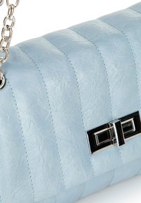 Borsa a spalla in pelle blu chiaro con sezioni cucite verticalmente e un dettaglio in metallo argentato. Dotata di una tracolla a catena per il trasporto.