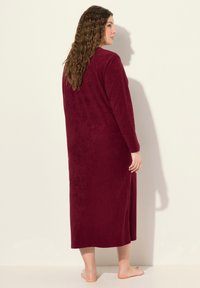 Lunga vestaglia color bordeaux realizzata in morbido tessuto peluche. Presenta maniche lunghe e un taglio dritto, che arriva a metà polpaccio. Design semplice e senza cuciture.