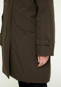 Brun overtøj med høj krave, store sidelommer og fastgjorte manchetter. Glat tekstur med en subtil glans. Minimalistisk design.