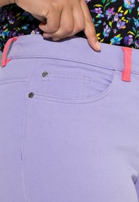 Jasnofioletowe spodnie z kontrastowymi różowymi akcentami, z przednią kieszenią, zamkiem błyskawicznym i srebrnym guzikiem. Gładka tekstura i dopasowany krój.