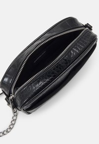 Czarna torebka wieczorowa ze sztucznej skóry o fakturze krokodyla, z srebrnym zamkiem błyskawicznym i łańcuszkiem. Wnętrze wyściełane miękką, ciemną podszewką. Kompaktowy i elegancki design.