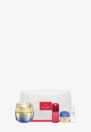 Cinq produits de soin Shiseido, comprenant des pots, un flacon de sérum, un petit tube et une trousse cosmétique matelassée blanche avec une étiquette rouge.