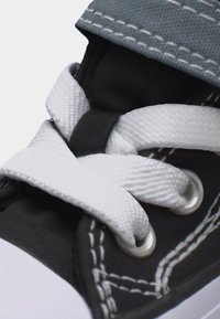 Κοντινό πλάνο μαύρου αθλητικού παπουτσιού με λευκά κορδόνια περασμένα μέσα από μεταλλικά οπές και ορατές λευκές λεπτομέρειες ραφής.