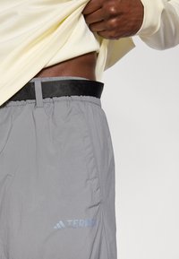 Οι γκρι ελαφριές παντελόνες διαθέτουν ελαστική μέση μ�ε μαύρη ζώνη. Στην πλαϊνή τσέπη υπάρχει ορατό το μπλε λογότυπο "TERREX".