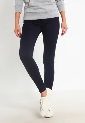 Vaqueros ajustados navy hechos de tela elástica, con textura suave y cinturilla estándar. Combinados con zapatillas blancas.