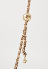 Χρυσή αλυσίδα πλεγμένη με ταπ (γκρίζο καφέ) δερμάτινες λωρίδες, η οποία διαθέτει μια στρογγυλή χρυσή διακοσμητική χάντρα και ένα μικρό χρυσό μπαλάκι στο τέλος.