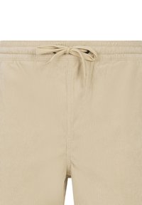 Beige ribbukse med elastisk linning og bundet snøre foran, som viser tekstur og syningsdetaljer.