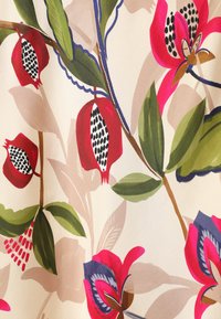 Tissu floral avec un fond crème, présentant de grandes fleurs roses et rouges, des feuilles vertes et des motifs de graines noirs et blancs. Texture lisse.