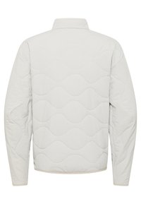 Veste matelassée gris clair avec un motif en vagues, dotée d'un col montant et de manches longues, fabriquée en matériau doux et texturé.