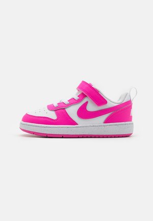 Scarpa sportiva bianca e rosa con strap in Velcro, caratterizzata da una suola testurizzata e da un grande logo Nike rosa sul lato.