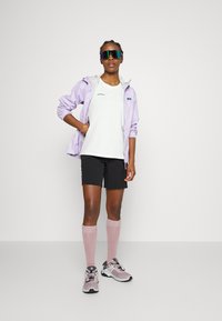 Light purple windbreaker with hood, white t-shirt, black shorts, pink knee-high socks, and gray sneakers with black accents.