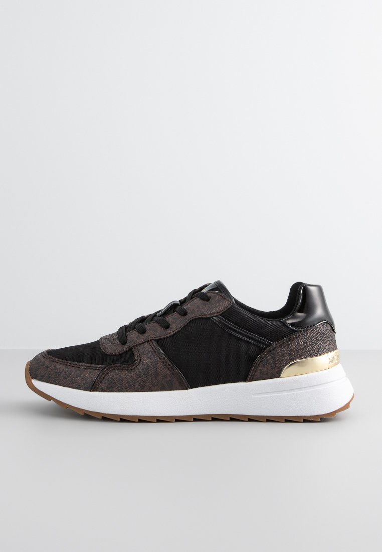 Sneaker noir et marron avec un motif texturé, semelle blanche, lacets noirs et détail doré au niveau du talon, présenté de côté droit sur une surface grise.
