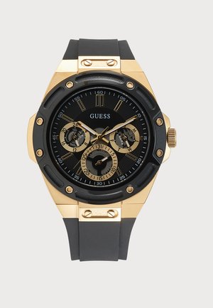 Черно и златно часовник Guess с кръгъл циферблат, три подциферблата, златни маркери и черна каишка със златни винтове на корпуса.