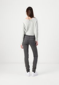 Suéter de punto gris claro, jeans oscuros de corte slim con bolsillos y zapatillas blancas. Diseño simple con una textura suave.