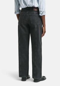 Jean noir en denim avec un design à jambe droite, cinq poches et une taille haute. Présente une surface texturée et des détails de couture minimaux.