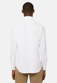 Witte langslijfshirt met een puntige kraag, knopenmanchetten en een afgeronde zoom, gemaakt van gladde stof. Details omvatten een plooi aan de achterkant.