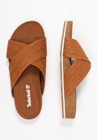 Sandali marroni con cinturini a croce, texture in suede, suola simile al sughero, accentatura bianca lungo il bordo e logo Timberland sulla soletta.