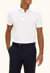 Vit kortärmad polo med knäppning, tillverkad av ett mjukt tyg. Matchas med marinblå byxor med sidofickor och knappknäppning.