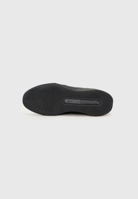Semelle de basket noire avec motifs circulaires et triangulaires et petit logo Nike swoosh au centre.