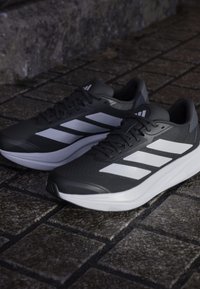 Black athletic shoes with white diagonal stripes, textured mesh upper, cushioned sole, featuring a smooth, rounded toe and lacing system.