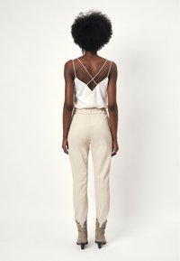 Witte satijnen top met gekruiste achterkant, gecombineerd met beige tapered broek en grijze enkelboots met studs.
