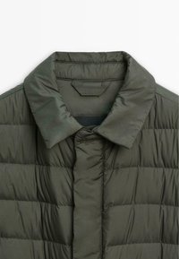 Olive green puffer jacket with a collared neckline, featuring quilted texture and a secure button closure down the front.