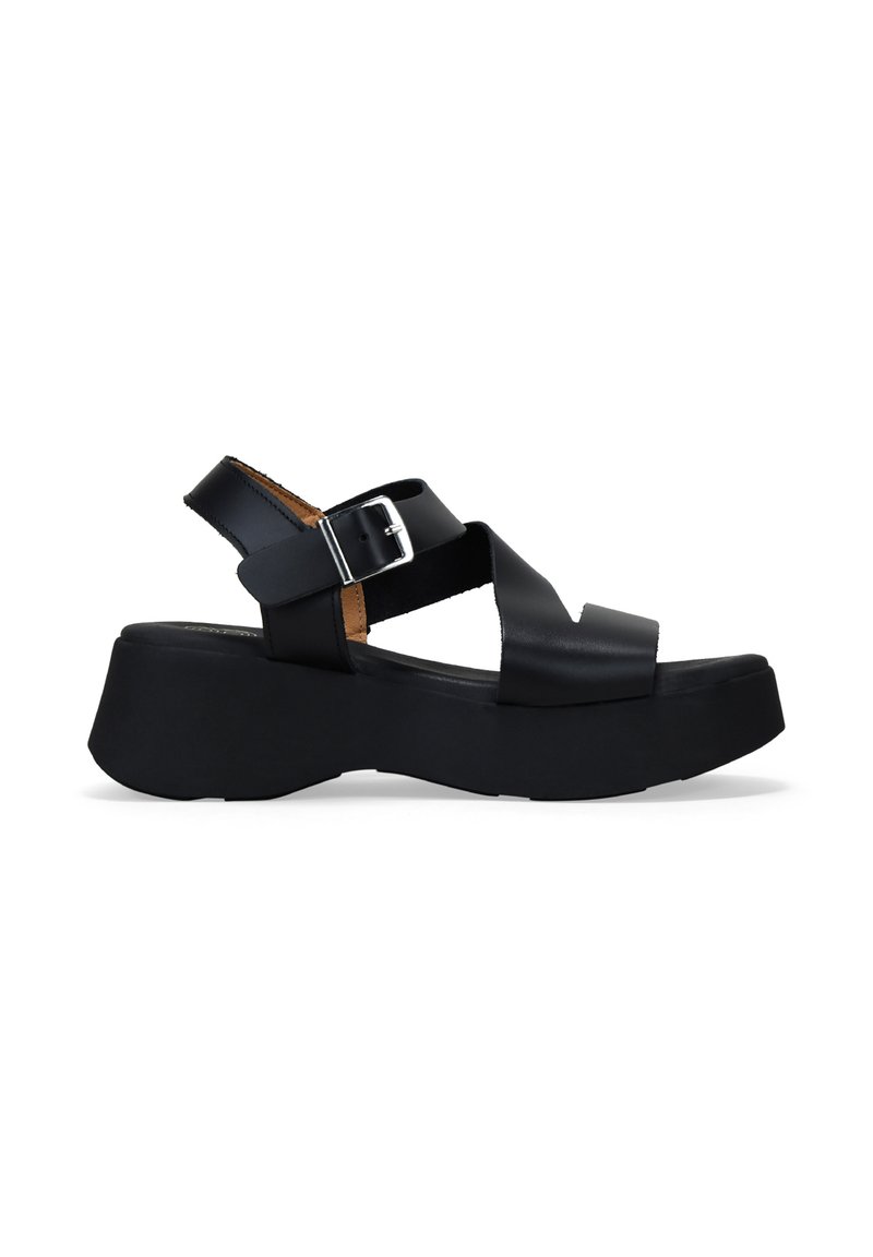Sandalias de plataforma negras con tacón cuadrado, que presentan tiras cruzadas y una hebilla lateral. El material parece suave con un acabado mate.