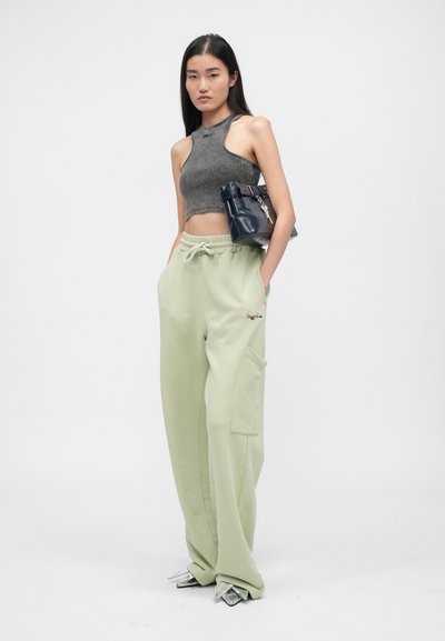 Sivý rebrovaný crop top, svetlozelené tepláky s vreckom a strieborné špicaté topánky; námornícky batoh so strapcom a detailom kľúča.