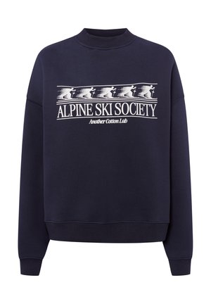 Marineblauwe crewneck sweater met witte afbeelding van vijf skiërs, tekst "ALPINE SKI SOCIETY" en kleinere tekst "Another Cotton Lab" eronder.
